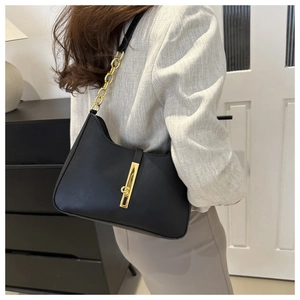 Detail of black underarm bag featuring glossy finish and gold chain strap on model