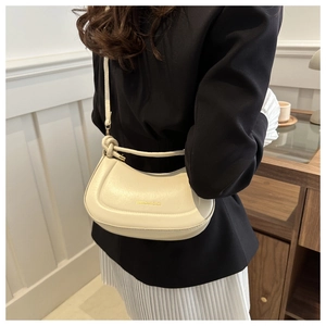 Close-up of cream half-moon bag with elegant curved stitching and gold lettering detail