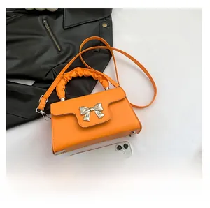 Detail of orange mini crossbody bag with silver bow buckle and wrinkled handle design