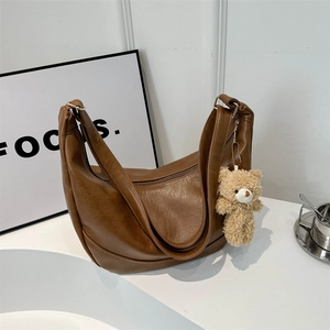 Vintage brown leather shoulder bag with a cute bear plush charm on a minimal desk