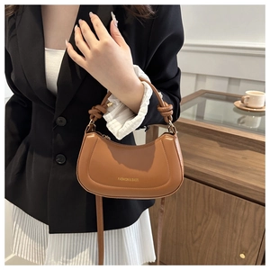 Caramel crescent bag with a knotted top handle and adjustable shoulder strap worn by a model