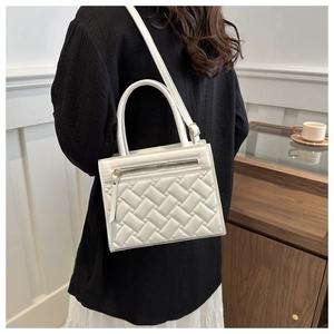 Detailed view of white quilted square handbag featuring double handles and crossbody strap