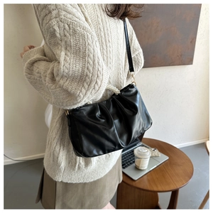 Detail of black pleated cloud bag featuring pearl handle and golden hardware accents