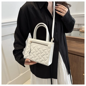 Close-up of white woven textured handbag worn by model in a modern minimalist setting