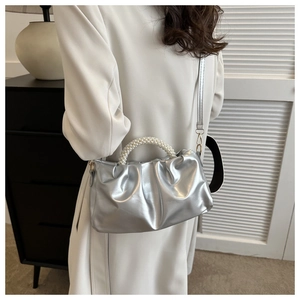 Detail view of silver pleated cloud bag with pearl handle on model's shoulder