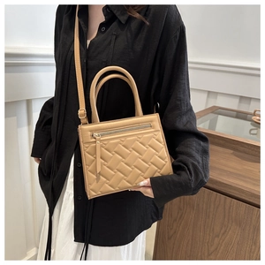 Detail of khaki quilted tote bag with woven texture on a white skirt outfit