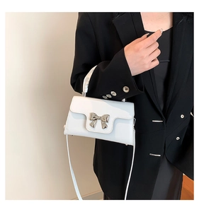 Detail of white glossy mini square bag featuring a silver metal bow buckle and handle
