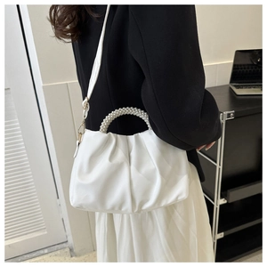 Detail view of white ruched handbag featuring elegant pearl bead handle and gold hardware