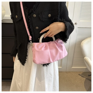 Pink pleated crossbody bag with elegant pearl handle shown in a lifestyle street setting