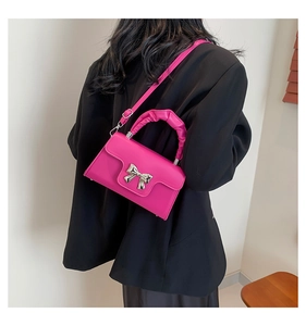 Detail of a bright pink small square crossbody bag with a silver metal bow on a black blazer