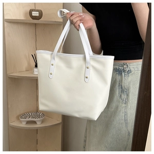 Close-up of minimalist cream tote bag with gold rivet details on the shoulder strap