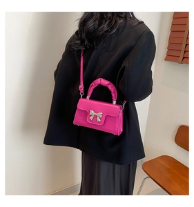 Detail of rose pink handbag with silver bow and adjustable shoulder strap on model