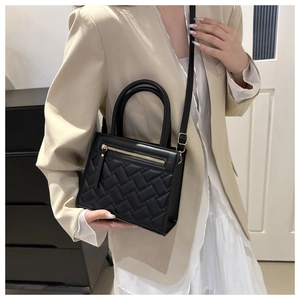 Detail of black quilted leather handbag with gold zipper shown on a model in a beige suit