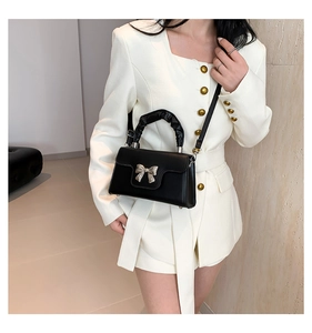 Detail of black mini crossbody bag featuring a silver bow buckle and ruched handle design