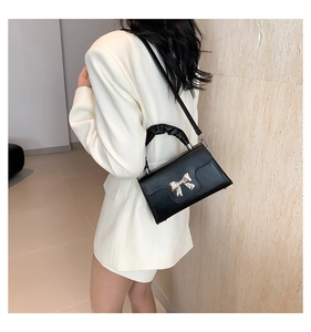 Close-up of black handbag with silver bow detail and pleated handle on white blazer