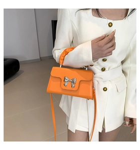 Detail showing an orange mini square bag with a silver bow and elegant ruched handle