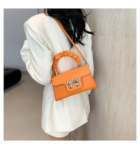 Orange crossbody bag featuring a silver bow detail and pleated handle on a model