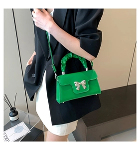 Close-up of bright green handbag featuring a silver bow accent and ruched handle