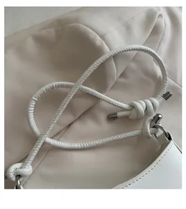 Detail of white shoulder bag featuring a unique knotted handle with silver metal end caps