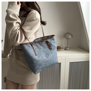 Blue denim tote bag with brown leather handles and gold studs worn over the shoulder