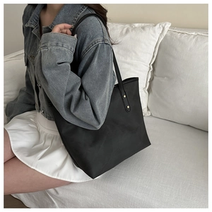 Detail of minimalist black tote bag with gold rivet accents on nylon material