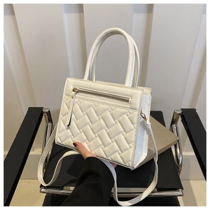 Close-up of white quilted square handbag featuring double handles and a long shoulder strap