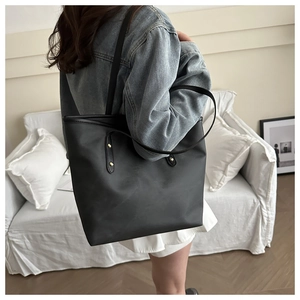 Detail of a large black leather tote bag with gold rivets worn on a shoulder