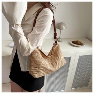 Close-up of a woven straw shoulder bag with brown leather strap worn by a model
