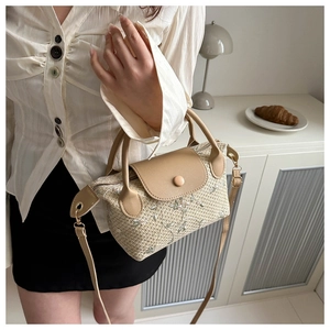 Detail of beige woven tote bag featuring floral embroidery and leather handles