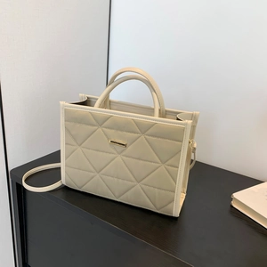 Beige quilted tote bag with golden plaque and crossbody strap on black wooden cabinet