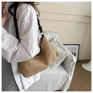 Close-up of woven straw hobo bag with black leather shoulder strap and knot detail