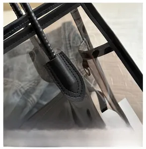 Detail view of transparent PVC tote bag featuring black leather trim and white letter print