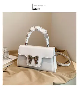 White shoulder bag featuring silver bow detail and pleated handle on beige background