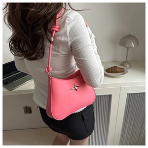 Pink underarm bag with silver star hardware and knot strap shown in lifestyle setting