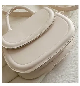 Detail view of cream white flap handbag with precise stitching and cylindrical handle