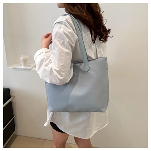 Modern light blue nylon tote bag worn by a model in a minimalist indoor setting