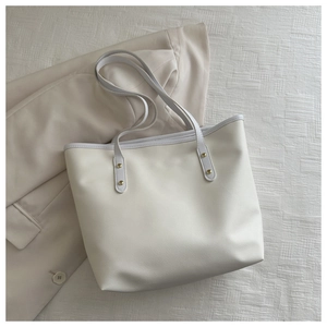 Detail of cream-white tote bag showing slim shoulder straps and gold rivet hardware