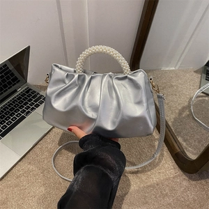 Silver pleated cloud handbag with pearl handle and crossbody strap in a modern setting