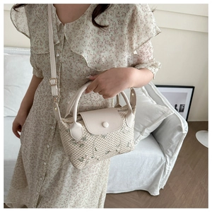 Detail of beige woven handbag featuring green floral embroidery and leather top handle