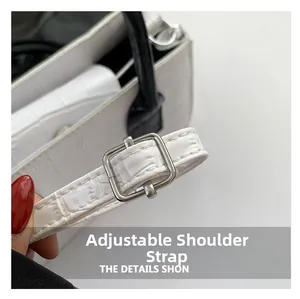 Close-up of adjustable shoulder strap with silver buckle on cream faux crocodile handbag
