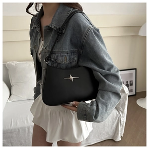 Close-up of a black matte shoulder bag with a silver star logo worn by a model in a room