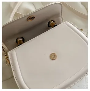 Close-up of bright gold magnetic clasp and cream-colored leather texture on saddle bag