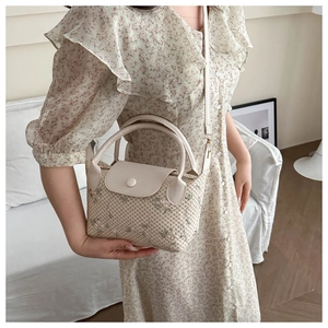 Close-up of beige woven straw handbag with floral embroidery and leather handle strap