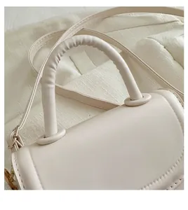 Detail of a beige saddle bag showing thick rounded handle and fine stitching craftsmanship