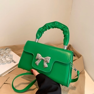 Green leather handbag with large silver bow buckle and ruched handle on casual background