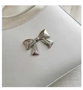 Close-up of a silver metal bow buckle on white leather texture for women's crossbody bag
