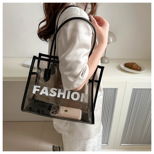 Detail view of a semi-transparent black PVC tote bag with white FASHION print and straps