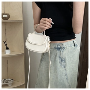 Minimalist white leather saddle bag with curved flap and elegant top handle detail