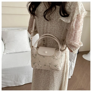 Detail of woven straw handbag featuring delicate floral embroidery and leather handle