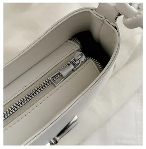 Detail of smooth silver metal zipper and precise stitching on white leather crossbody bag
